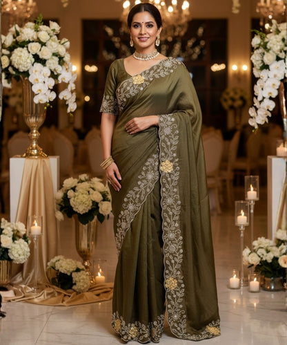 Woman in a green saree with floral patterns in an elegant indoor setting.