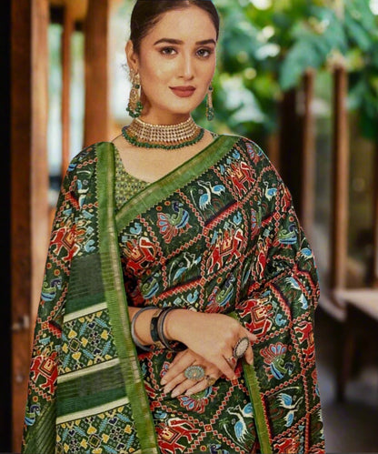 Woman wearing a traditional printed saree with a green border against a decorative wall.