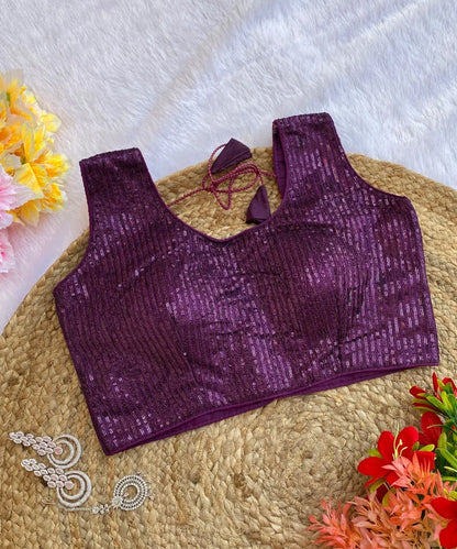 Wine colored sequin blouse with a round neck and sleeveless design, displayed on a beige background with flowers and jewelry in the periphery.