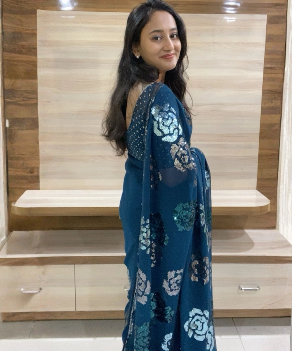 Woman wearing a blue saree with white patterns in a room with wooden furniture.