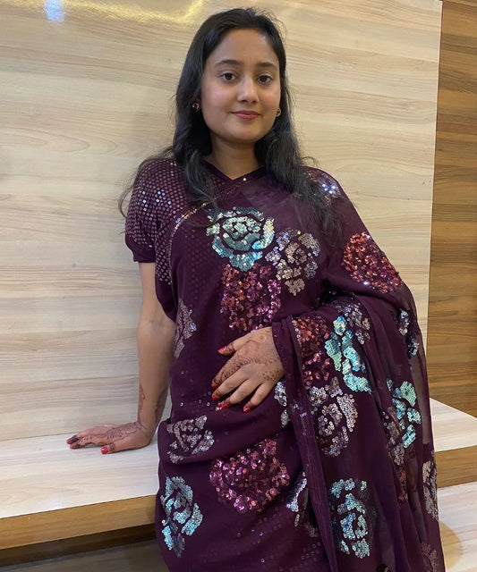 A woman posing in a purple saree with floral sequin motifs and a sequin border.