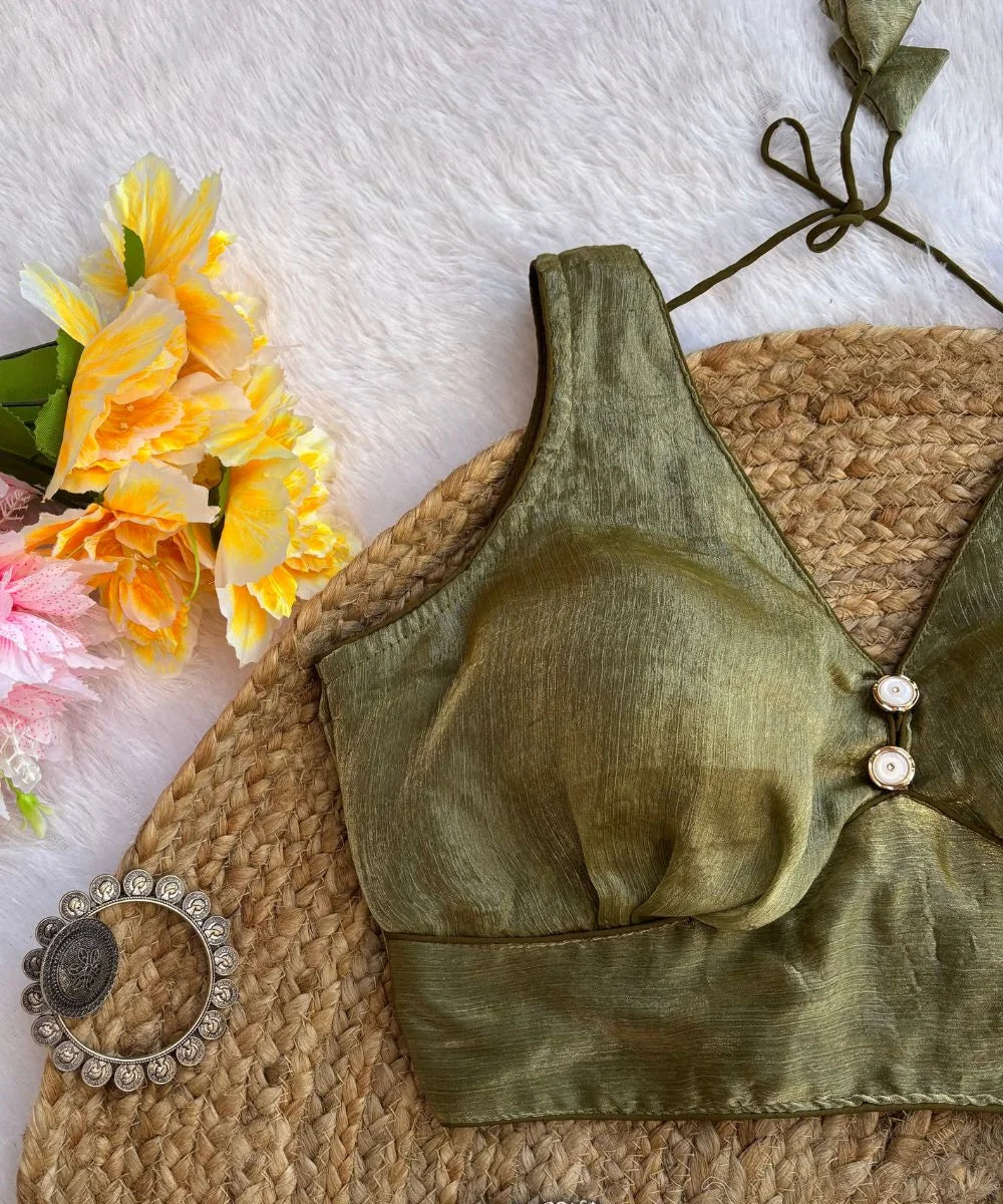 A moss green sleeveless blouse with a deep V-neck, displayed on a beige background with flowers and decorative earrings in the peripherals.
