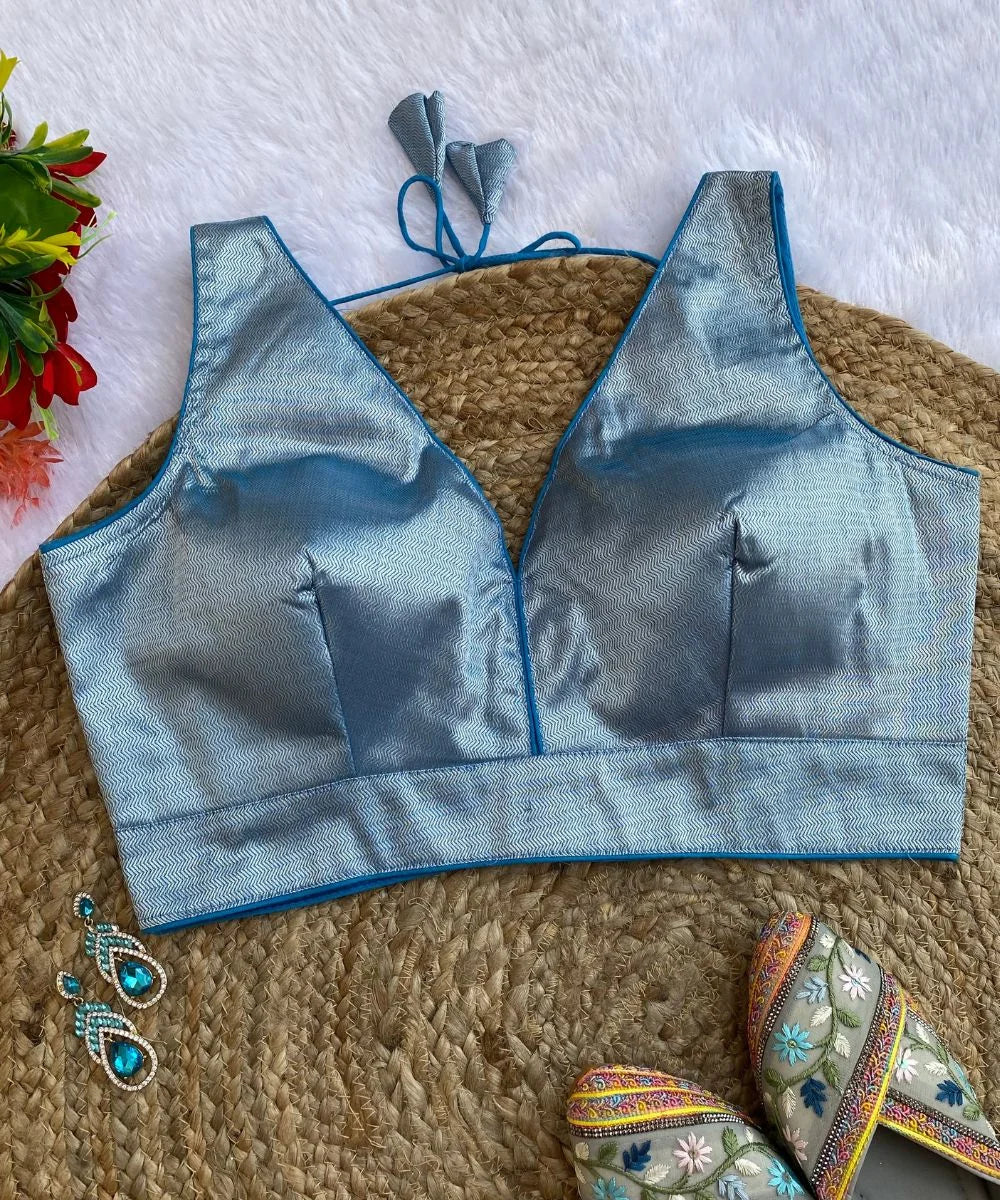 Sky-blue colored self-printed blouse with a deep V-neck and sleeveless design, accompanied by decorative earrings and a traditional sandal.