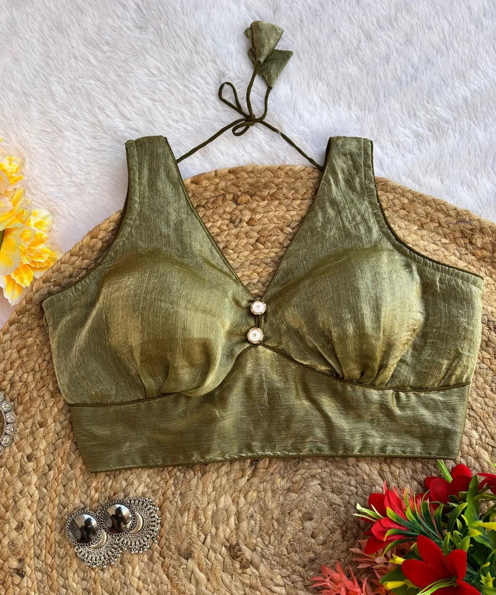 A moss green sleeveless blouse with a deep V-neck, displayed on a beige background with flowers and decorative earrings in the peripherals.