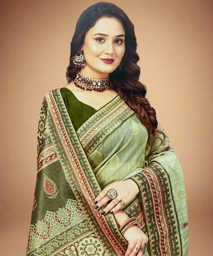 Woman wearing a green saree with intricate patterns and jewelry against a brown background