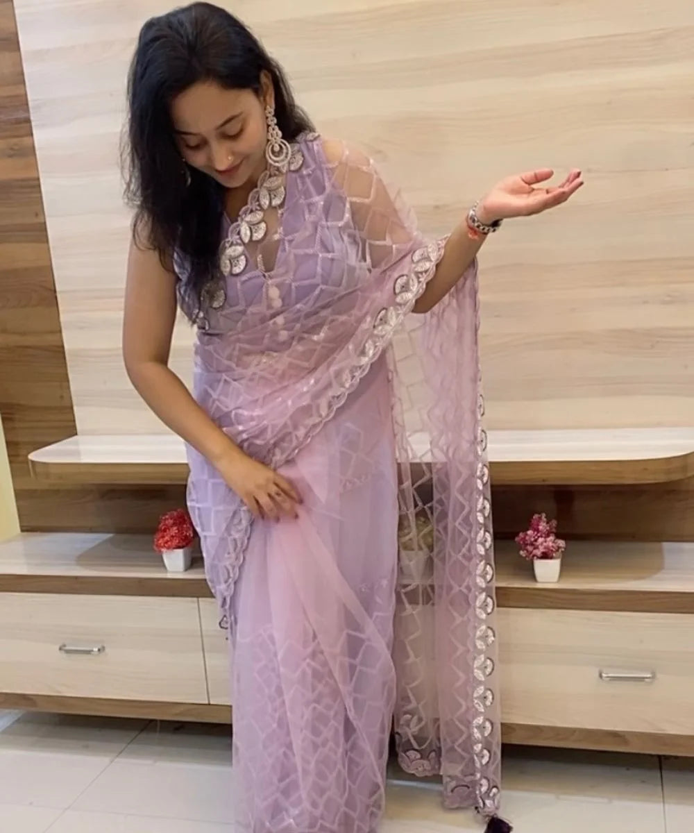 A woman showcasing a lavender net saree with sequin checkered pattern and scalloped border with intricate mirror and thread work.
