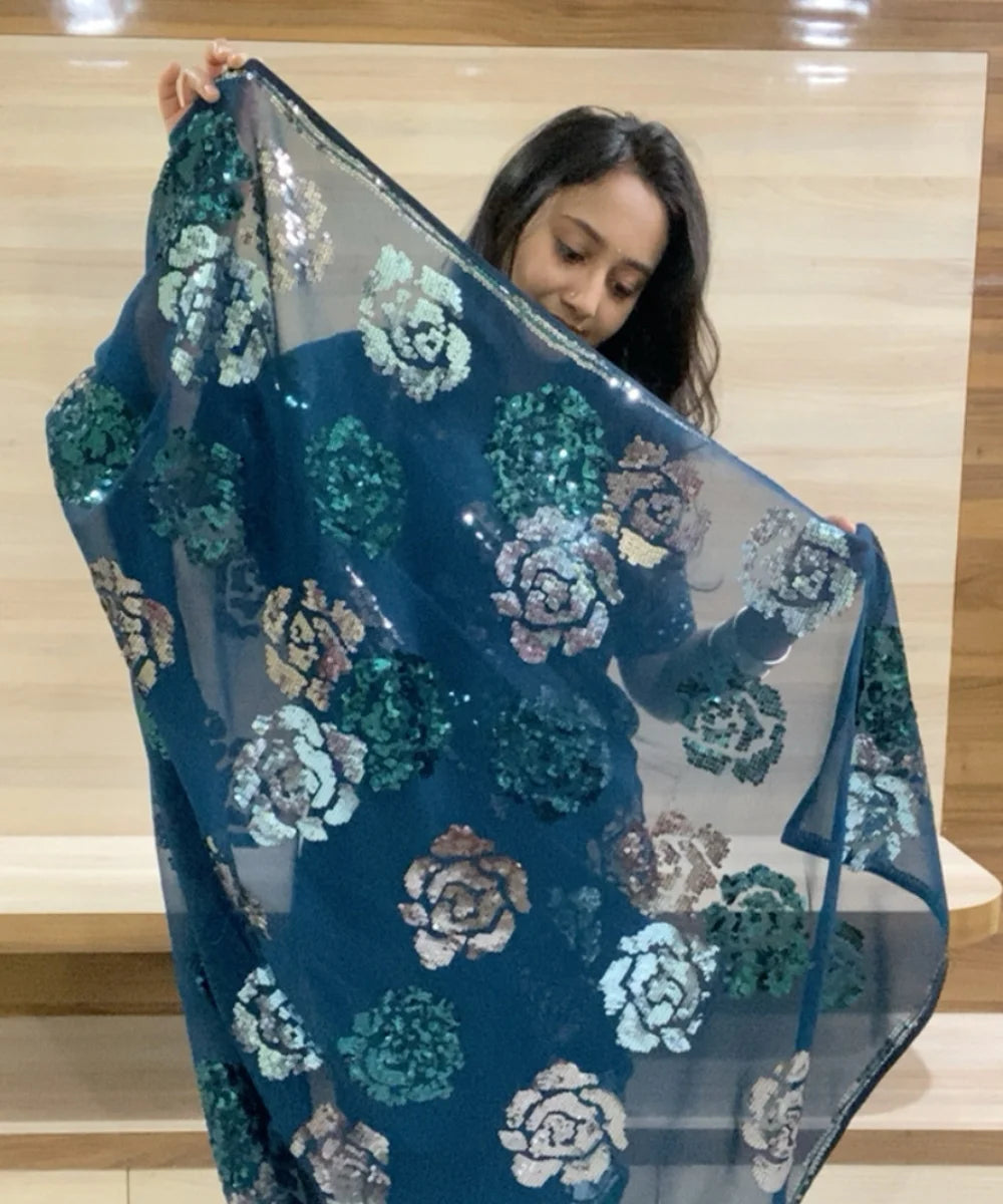 Woman holding a blue floral sequin fabric against a wooden background