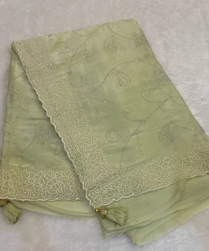 A green saree with floral embroidery and tassel details, laid flat.